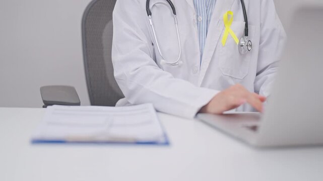doctor using laptop and report notes on notebook for Gold Yellow Ribbon for concept of September Childhood Awareness month, July Sarcoma, bone and bladder, support survivor. World Cancer day