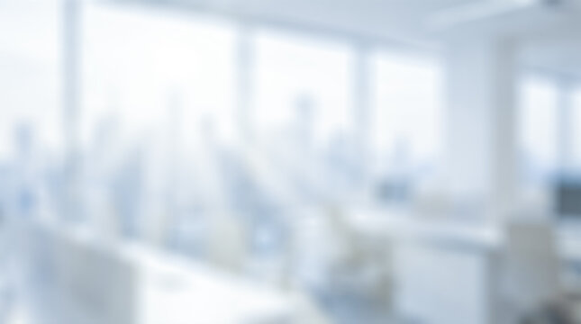 Blurred background showing empty open plan corporate office interior featuring white desks beside large windows revealing bright sunlight illuminating commercial business workspace