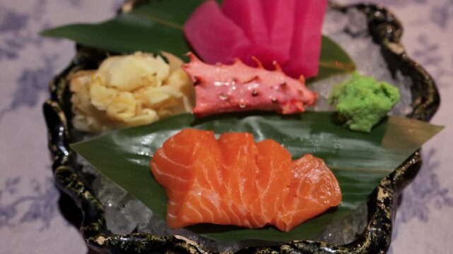 A close up shot of a beautifully presented sashimi platter on a bed of ice, with salmon, tuna, crab leg, pickled ginger, and wasabi, rotating on a table.
