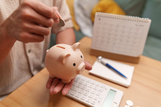 Man placing a coin into a piggy bank beside a calculator and calendar, representing budgeting, scheduled saving, retirement planning, and long-term financial security.