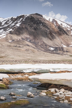 Landscape in the high Pamirs with rocky peaks and a river in a valley with melting snow. Panorama of rocky mountains on a sunny day and glaciers in a river valley
