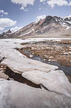 Landscape in the high Pamirs with rocky peaks and a river in a valley with melting snow. Panorama of rocky mountains on a sunny day and glaciers in a river valley