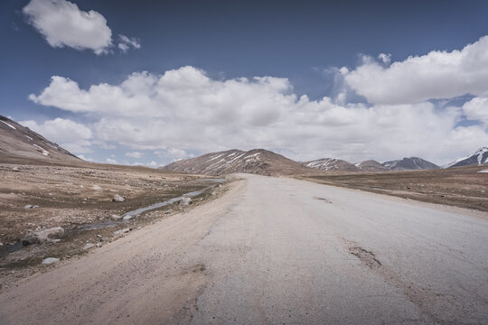 Dusty road of the Pamir Highway winds and twists in the valley of the Tien Shan mountains in Tajikistan in Pamir, landscape in the high desert mountains for background
