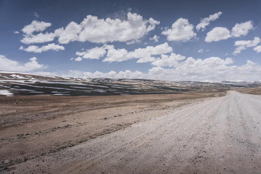 Dusty road of the Pamir Highway winds and twists in the valley of the Tien Shan mountains in Tajikistan in Pamir, landscape in the high desert mountains for background