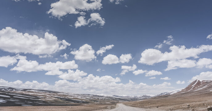 Dusty road of the Pamir Highway winds and twists in the valley of the Tien Shan mountains in Tajikistan in Pamir, landscape in the high desert mountains for background