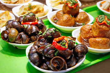 Fototapeta premium Traditional Shanghai dishes of spicy river snails and braised meatballs served in bowls at a street food market, China