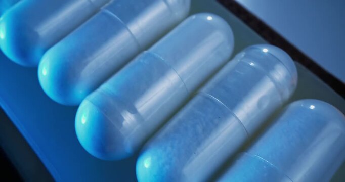 Tracking shot of translucent capsules sliding across blister pack on conveyor belt in production, macro probe lens.