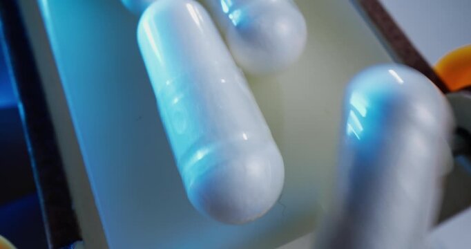 Tracking shot of white capsules rotating and sliding on conveyor line inside pharmaceutical packaging factory, macro probe lens.