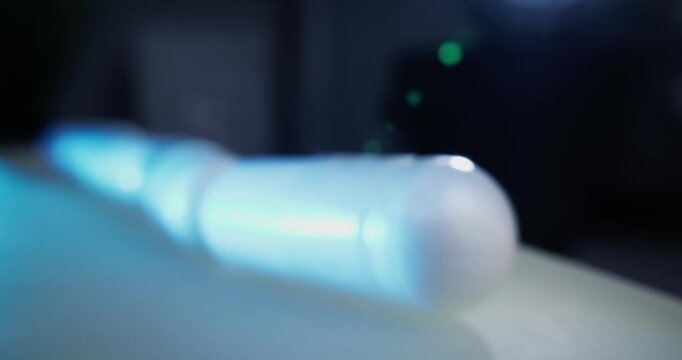 Slow motion close up of glowing capsule tube sliding on tabletop blue light on conveyor belt in production, macro probe lens.
