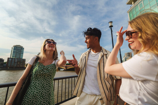 Diverse friends laughing, having fun outdoors by a river, celebrating youth and friendship