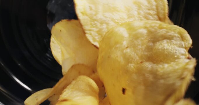 Slow motion potato chips tumbling and colliding inside conveyor in food production, macro probe lens.
