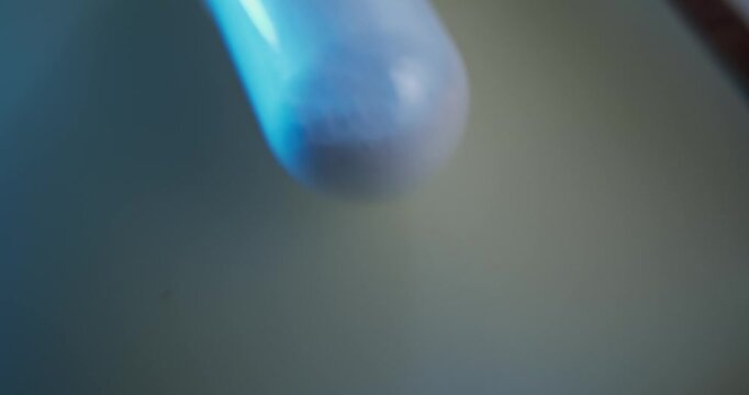 Slow motion close up of translucent capsule rotating under blue light in laboratory setting, macro probe lens.