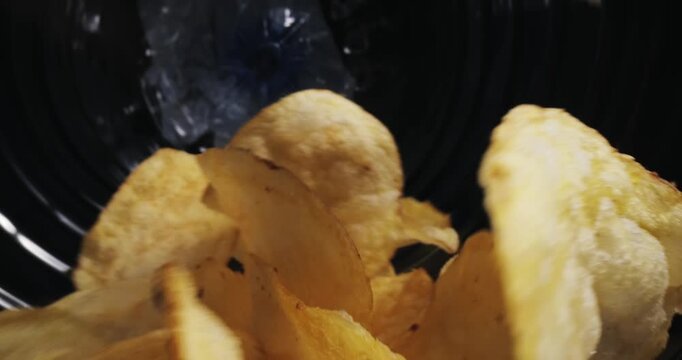 Slow motion potato chips tumbling inside crinkled snack bag interior on kitchen counter, macro probe lens.