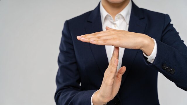 Businesswoman in a formal dark suit making a time-out hand gesture against a neutral studio background.