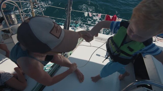 Kids wear lifejackets and sit on the deck of a sailing boat moving fast in the sea