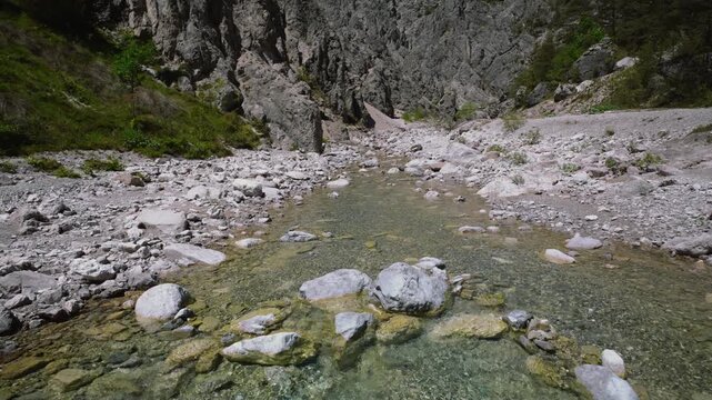 Crystal clear alpine river water flowing over gravel with mountains behind, Friulian Dolomites, Italy