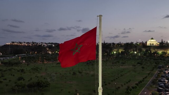Blue hour drone view of the Moroccan flag with Hassan Tower and the V Mausoleum in Rabat, showcasing Morocco's national identity and UNESCO World Heritage landmark.