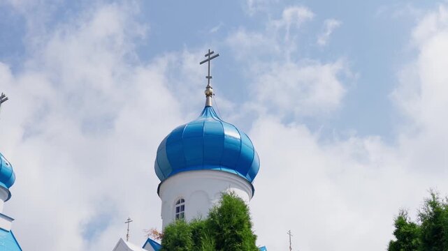 Close up panning shot showing ornate blue dome and golden cross of Saints Boris and Gleb Cathedral under bright sunny sky with clouds in Daugavpils Latvia.
