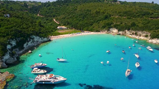 Aerial descend over the beautiful turquoise bay of Voutoumi Beach, where luxury yachts anchor in pristine Ionian waters, Antipaxos Island, Greece