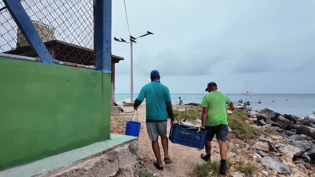 Local fishermen carry freshly caught fish from the shoreline to a processing station in a traditional Caribbean fishing community supporting sustainable seafood.