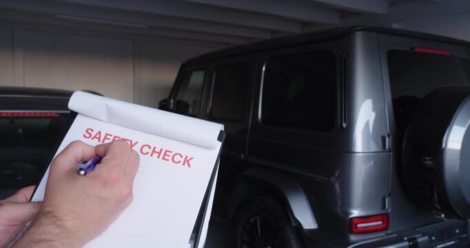 Person completing a car safety check checklist next to a vehicle, documenting inspection results before driving and verifying road safety.