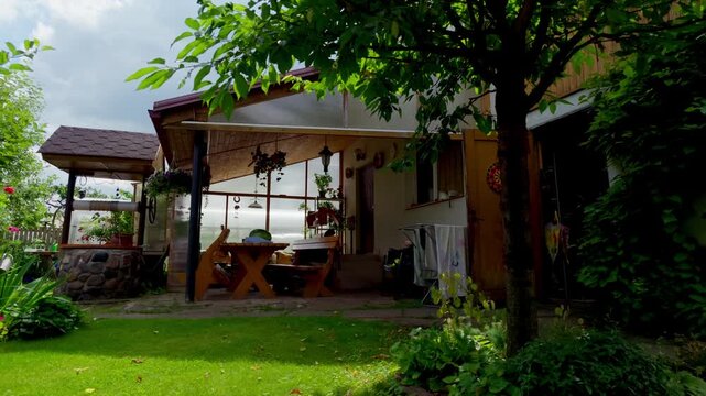 Tranquil private garden features rustic wooden furniture under shade of leafy tree next to stone well. Summer day scene of peaceful courtyard setup for relaxation.