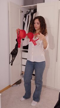 A woman compares two bras while deciding what to wear in front of her wardrobe.