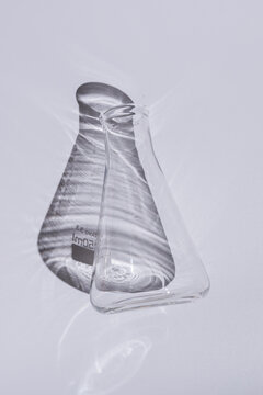 glass laboratory flask isolated on white background, transparent scientific equipment with dramatic shadow, minimalist chemistry concept with copy space