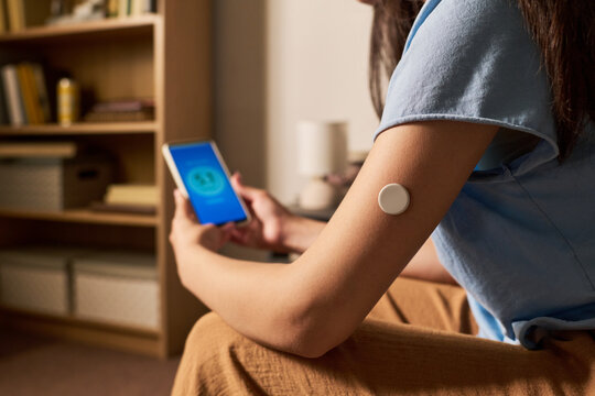 Young adult woman with diabetes checking glucose level using continuous monitor sensor on arm and smartphone. Image ideal for digital health and modern medical technology marketing