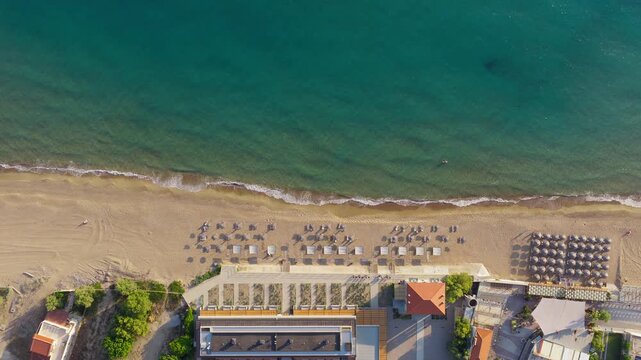 Top-down of an organized beach club at Kourouta Beach in Ilia, Greece, with rows of sun loungers, umbrellas, beachfront facilities, and calm turquoise water meeting the sandy shore