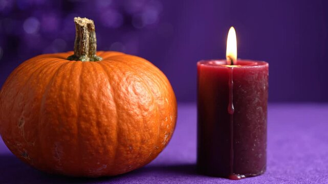 Small orange pumpkin and lit red candle on purple background, Halloween still life with wax drip and soft bokeh