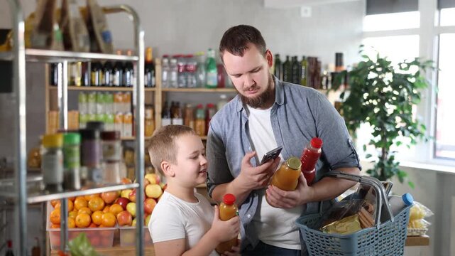 Focused tween boy with friendly young father scanning barcodes on bottles with fruit juices with phone while shopping in supermarket, checking product information and price 