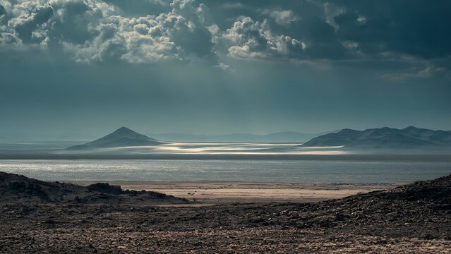 Dramatic moody landscape of a vast desert salt flat with distant mountains under a dark stormy sky.
