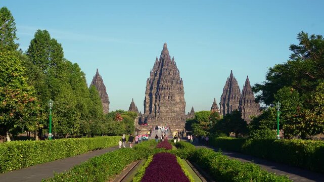 Colorful flower gardens and a symmetrical pathway lead toward the majestic central tower of Prambanan Temple near Yogyakarta.