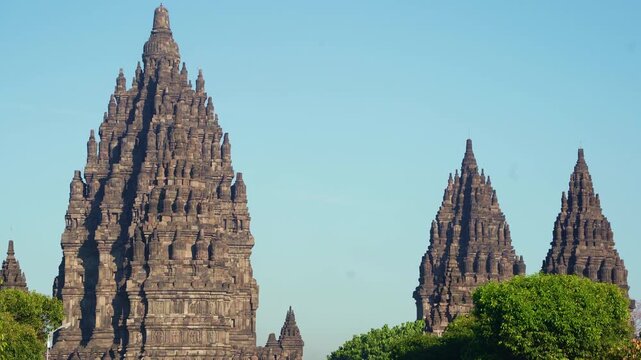 Majestic Prambanan Temple towers rise above green trees beneath a brilliant blue sky in Central Java, Indonesia.