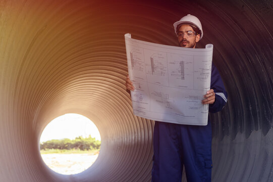 A male engineer in an orange suit is inspecting the integrity and safety of a pipeline.