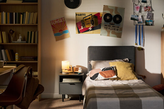 Empty teenager bedroom showing single bed, nightstand with lamp, and posters on wall. Image suitable for youth lifestyle marketing, interior design inspiration, or real estate staging
