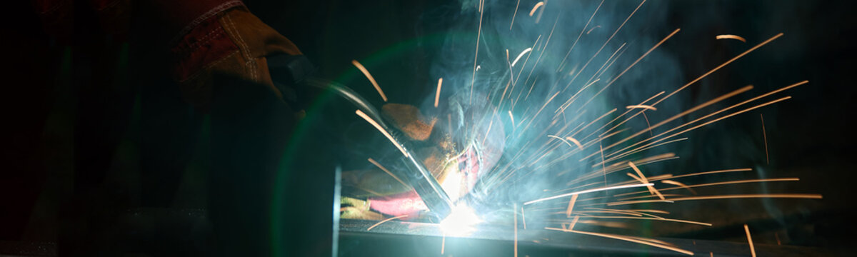 Close up of welder hands in protective gloves welding metal with bright sparks flying. Image represents industrial manufacturing and is suitable for vocational training promotion