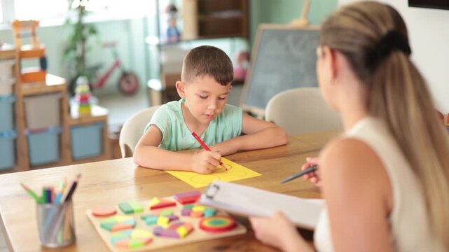 Boy draws or pass round geometric shapes on yellow sheet with pencil. Exercises and tasks for development of fine motor skills. Developing and maintaining skills for children with special needs 