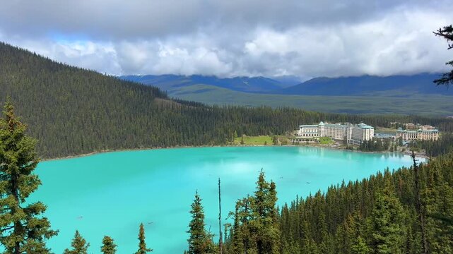 Beautiful view on the Lake Louise in National Park of Banff, Canada. Panoramic view of a turquoise lake bordered by lush green forests and mountains, with a hotel visible on the shoreline