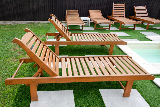 Wooden sun loungers lined beside a pool on artificial grass at a modern hotel patio