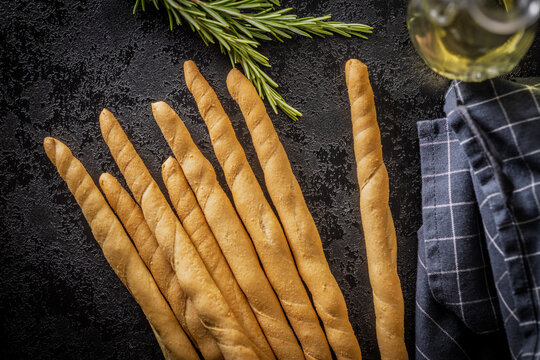Italian Grissini Breadsticks with Fresh Rosemary and Olive Oil on Dark Rustic Surface