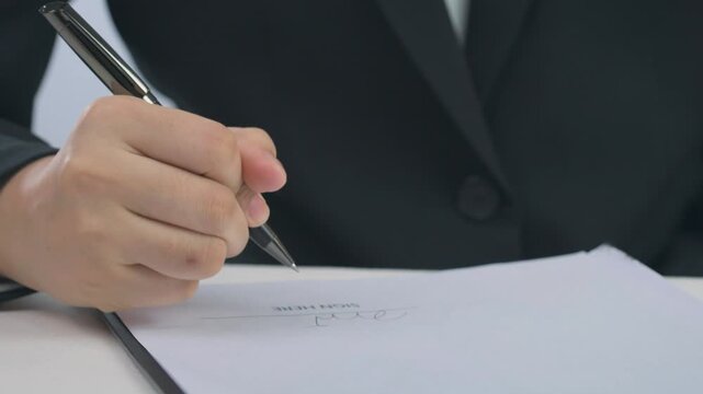 Determined hand holding silver pen to sign mortgage contract on paper achieving proud home ownership goal with legal agreement document