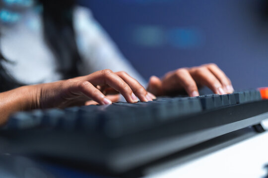 Close-up of hands typing on a mechanical keyboard in blue light at night, an anonymous image of coding, software development and technology.