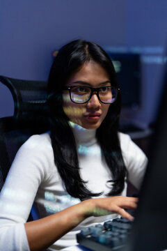Asian woman programmer with glasses typing on keyboard while working with AI assisted code, collaborating with artificial intelligence to write and fix software at night