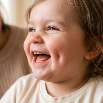 Toddler is laughing joyfully while showing a bright smile with dimples in a warm and comfortable indoor living space.