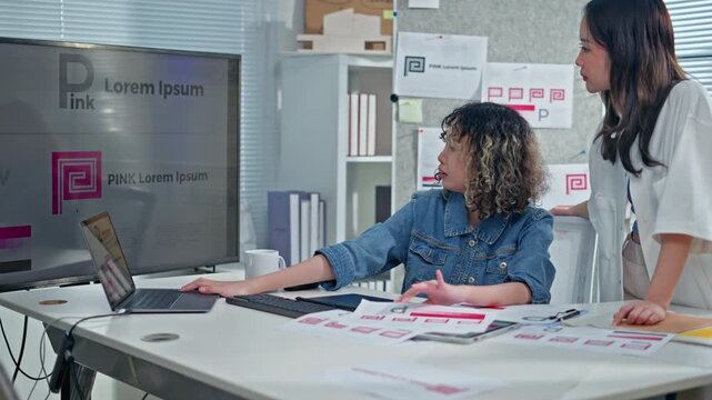 Two Asian Designer woman meeting brainstorming ideas about design logo,discuss on tablet and paper,female colleagues working together design banner logo in office.Graphic Design and Designer concept
