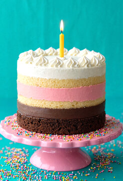 Delicious multilayered birthday cake with colorful sprinkles and a lit candle on top