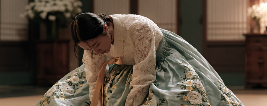 Korean woman kneeling on the floor in an elegant hanbok with her hands gently folded, humble posture symbolize modesty, politeness, and cultural values.