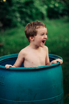 Little Boy Laughing and Playing Inside Large Blue Barrel